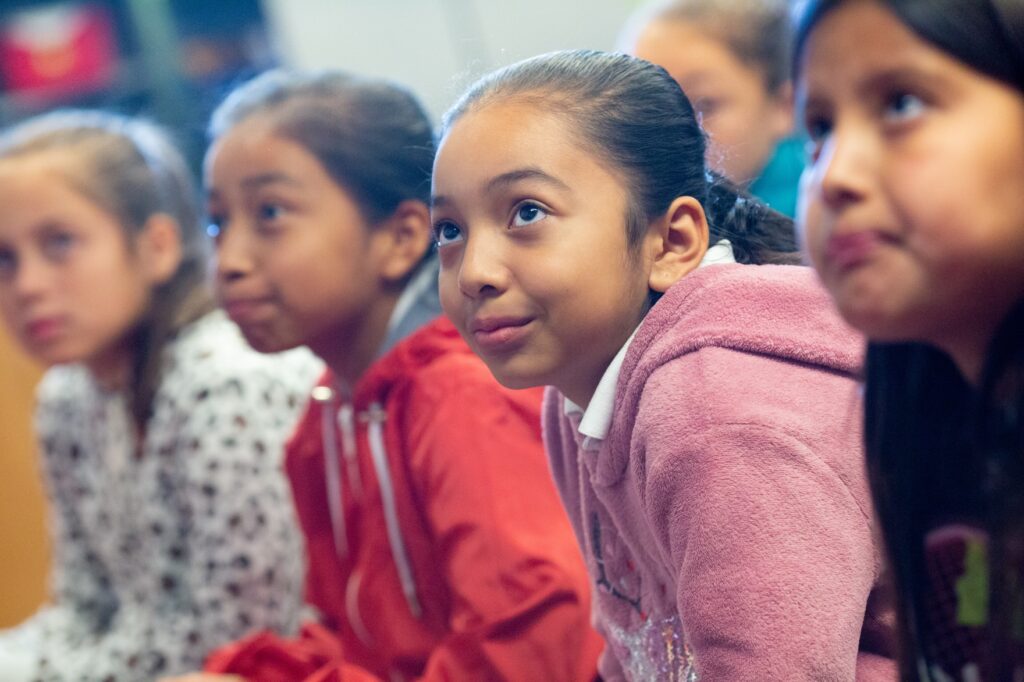 A group of elementary school girls listens to their teacher during class.